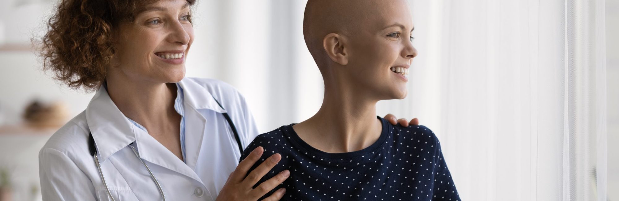 Smiling Caucasian doctor or nurse support comfort millennial woman struggle with oncology. Happy GP and optimistic female cancer patient look in distance dream of illness recovery or remission.